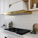 Modern kitchen setting featuring the Forno Vittorio 48-Inch Wall Mount Range Hood in white with antique brass trim, installed above a wide cooktop. The hood complements the bright cabinetry and upscale decor, blending elegance with high-performance ventilation.